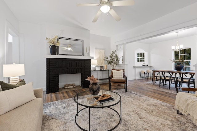 living room with a fireplace, wood-type flooring, and ceiling fan with notable chandelier