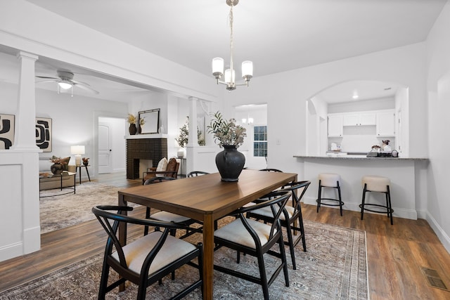 dining room with dark hardwood / wood-style flooring, a fireplace, and ceiling fan with notable chandelier