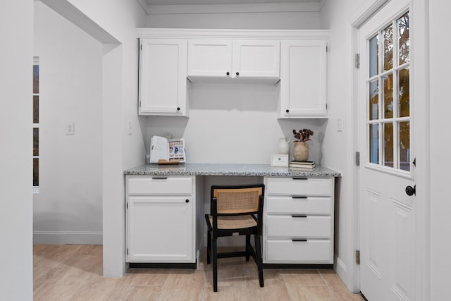 kitchen featuring light stone countertops, built in desk, white cabinets, and light hardwood / wood-style floors