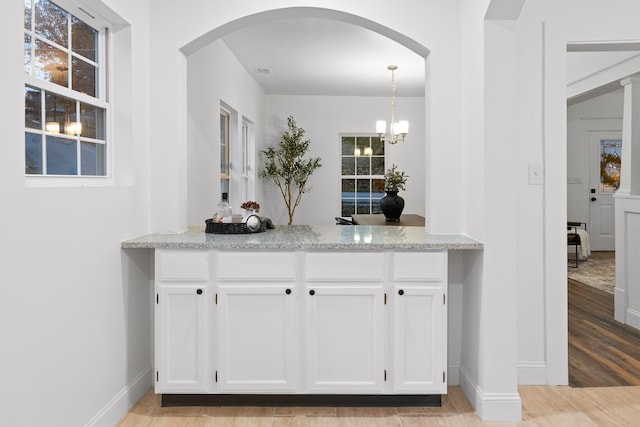 bar featuring a chandelier, light wood-type flooring, white cabinetry, and light stone counters