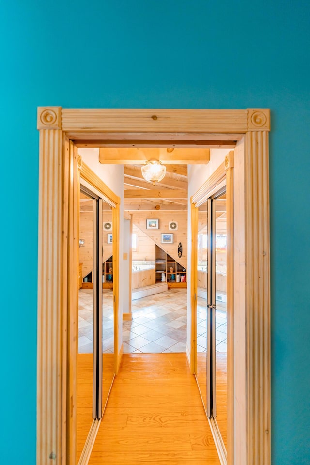 corridor with beam ceiling, wood finished floors, and wood walls