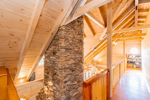 corridor with wooden walls, vaulted ceiling with beams, wood ceiling, and light wood-style floors