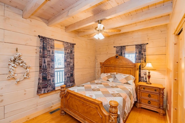 bedroom with visible vents, wood walls, beamed ceiling, and multiple windows