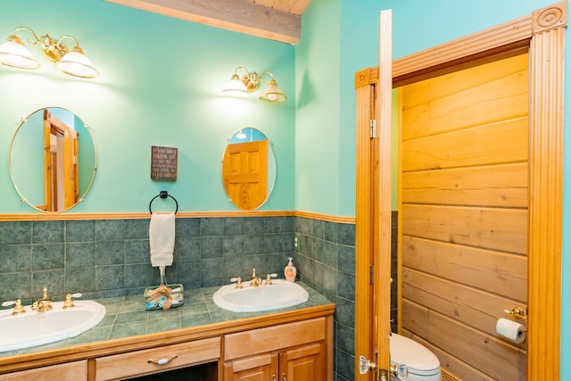 full bath with a sink, toilet, tile walls, and double vanity