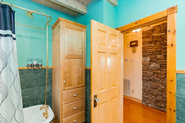 bathroom featuring visible vents, beamed ceiling, shower / bath combo, wood finished floors, and tile walls