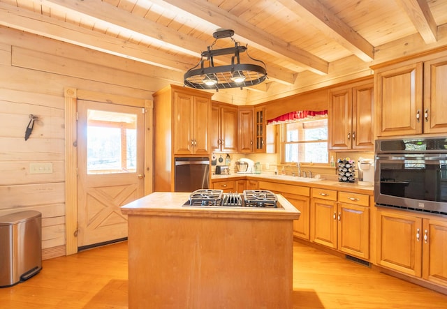 kitchen featuring a sink, gas cooktop, a kitchen island, wooden walls, and stainless steel oven