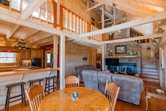 dining space with wooden walls, wood finished floors, beam ceiling, a stone fireplace, and wooden ceiling