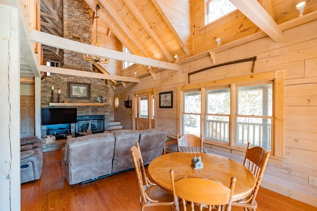 dining room with wooden walls, wood finished floors, a stone fireplace, wooden ceiling, and beamed ceiling