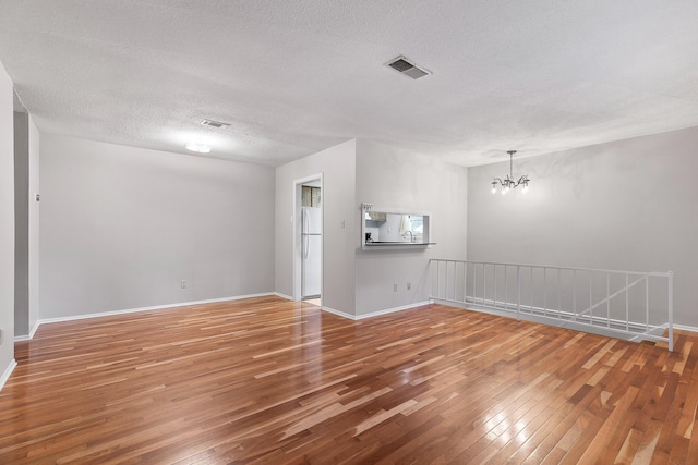 unfurnished room with a textured ceiling, hardwood / wood-style flooring, and an inviting chandelier