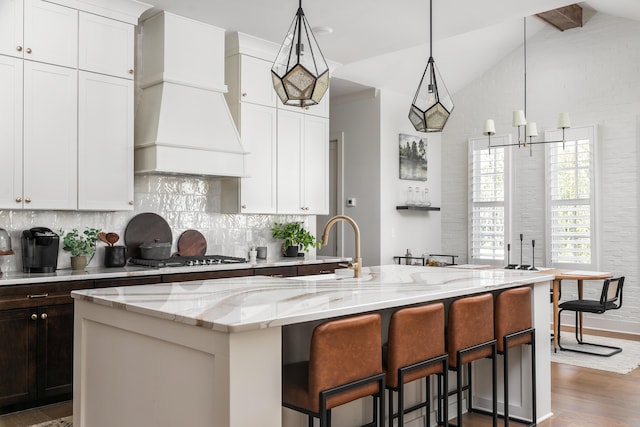 kitchen featuring custom range hood, white cabinetry, stainless steel gas cooktop, and lofted ceiling