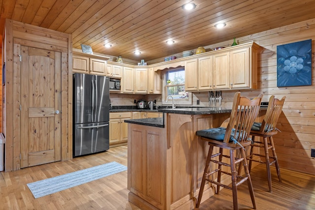 kitchen featuring wood walls, light brown cabinets, stainless steel fridge, light wood-type flooring, and kitchen peninsula