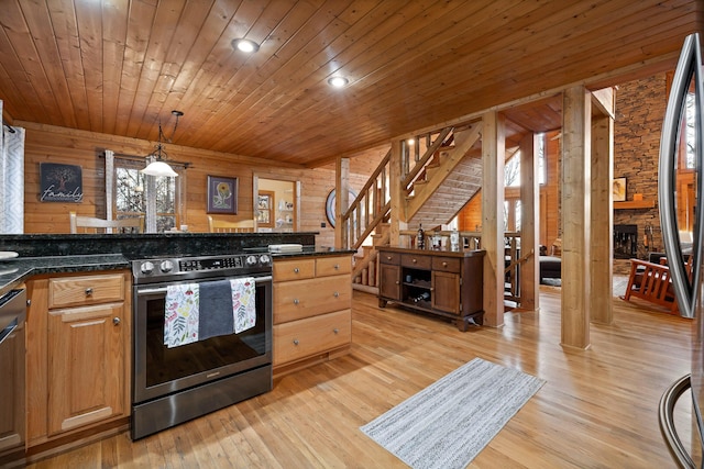 kitchen featuring pendant lighting, dark stone counters, wooden walls, a fireplace, and stainless steel appliances