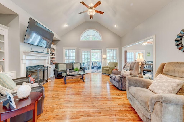 living room with built in shelves, ceiling fan, a tile fireplace, high vaulted ceiling, and light hardwood / wood-style flooring