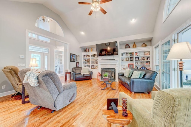 living room with a tiled fireplace, high vaulted ceiling, light hardwood / wood-style floors, and ceiling fan with notable chandelier