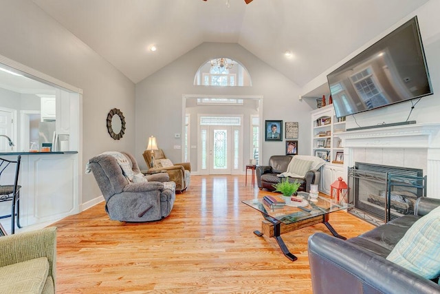 living room with a tile fireplace, ceiling fan, high vaulted ceiling, and light wood-type flooring