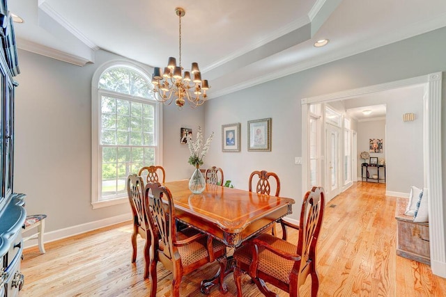 dining area with a chandelier, ornamental molding, a tray ceiling, and light hardwood / wood-style flooring