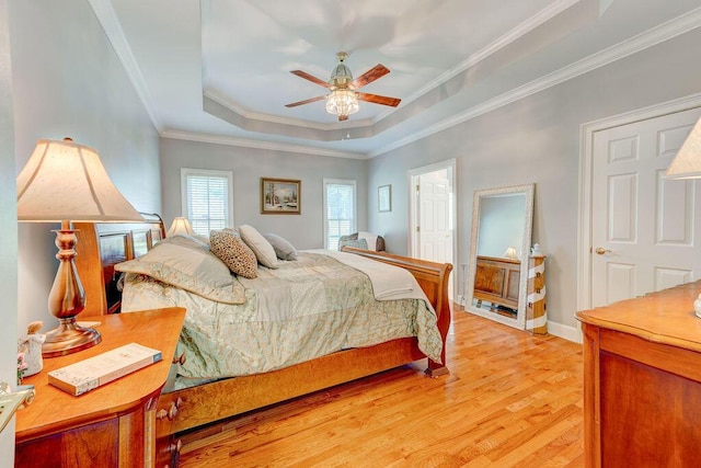 bedroom featuring a raised ceiling, ceiling fan, crown molding, and light wood-type flooring