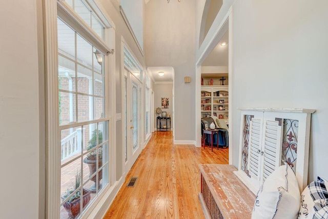 hallway featuring a high ceiling, light wood-type flooring, and built in features