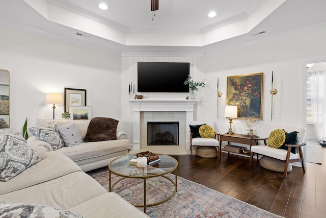 living room with a raised ceiling, a fireplace, dark hardwood / wood-style floors, and ornamental molding