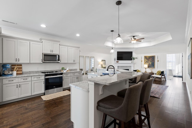 kitchen featuring light stone counters, an island with sink, decorative light fixtures, and appliances with stainless steel finishes