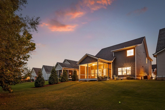 back house at dusk featuring a lawn, a sunroom, and central AC