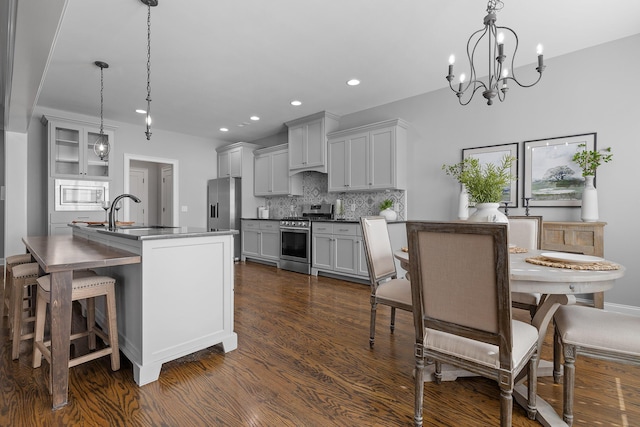 kitchen featuring an island with sink, dark hardwood / wood-style floors, decorative light fixtures, and appliances with stainless steel finishes