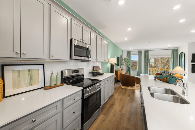 kitchen with gray cabinetry, sink, appliances with stainless steel finishes, tasteful backsplash, and dark hardwood / wood-style flooring