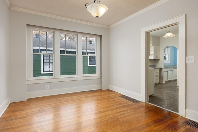 empty room with a textured ceiling, hardwood / wood-style flooring, and crown molding