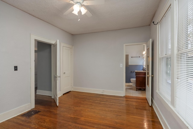 unfurnished bedroom featuring ceiling fan, wood-type flooring, a textured ceiling, and ensuite bath