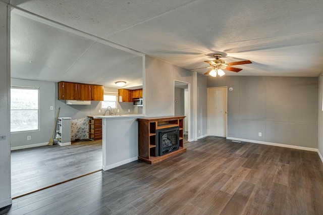 unfurnished living room with sink, vaulted ceiling, ceiling fan, a textured ceiling, and dark hardwood / wood-style flooring