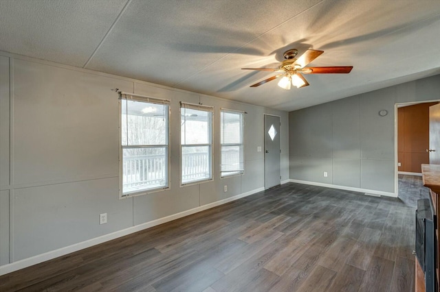 spare room featuring ceiling fan, a fireplace, dark wood-type flooring, and a textured ceiling