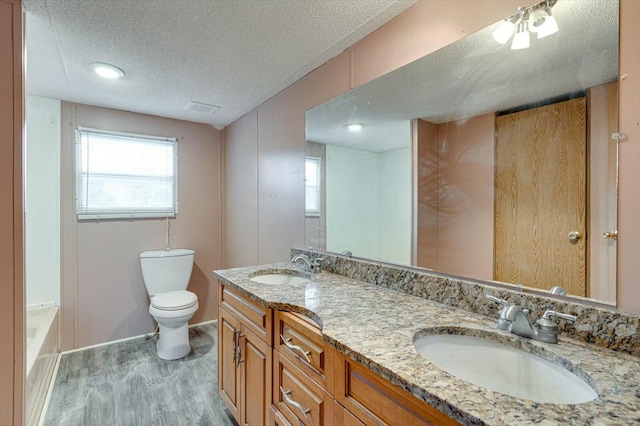 bathroom with a textured ceiling, vanity, hardwood / wood-style flooring, toilet, and a tub