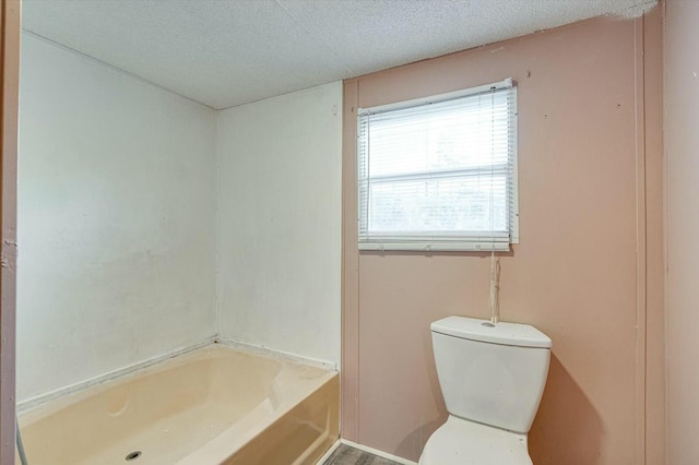 bathroom featuring a tub to relax in, a textured ceiling, and toilet