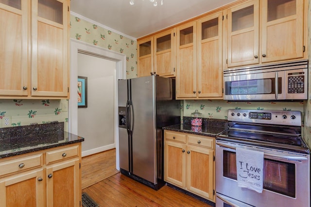 kitchen with dark stone countertops, ornamental molding, stainless steel appliances, and light hardwood / wood-style floors