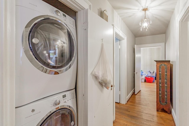 laundry area with light wood-type flooring, stacked washing maching and dryer, and a chandelier