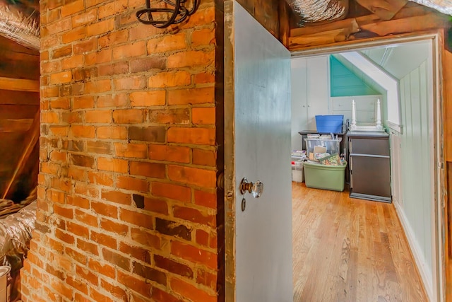 hall with light wood-type flooring and brick wall