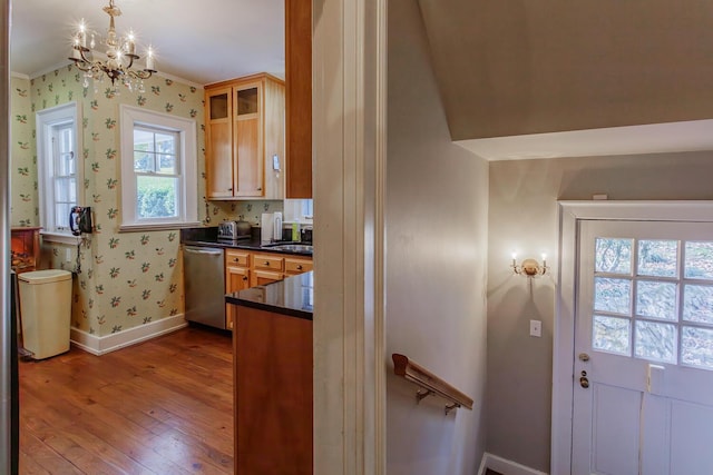 kitchen with hanging light fixtures, light hardwood / wood-style flooring, stainless steel dishwasher, ornamental molding, and a notable chandelier