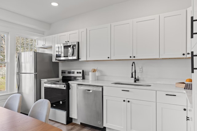 kitchen with hardwood / wood-style floors, white cabinetry, sink, and stainless steel appliances