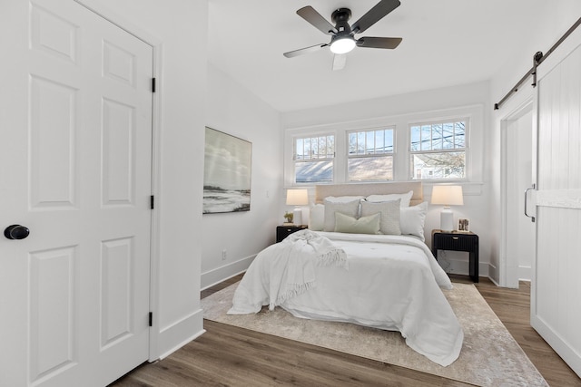 bedroom with dark hardwood / wood-style floors, a barn door, and ceiling fan