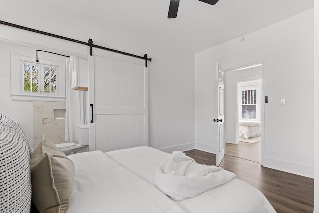 bedroom with connected bathroom, a barn door, ceiling fan, and dark hardwood / wood-style floors