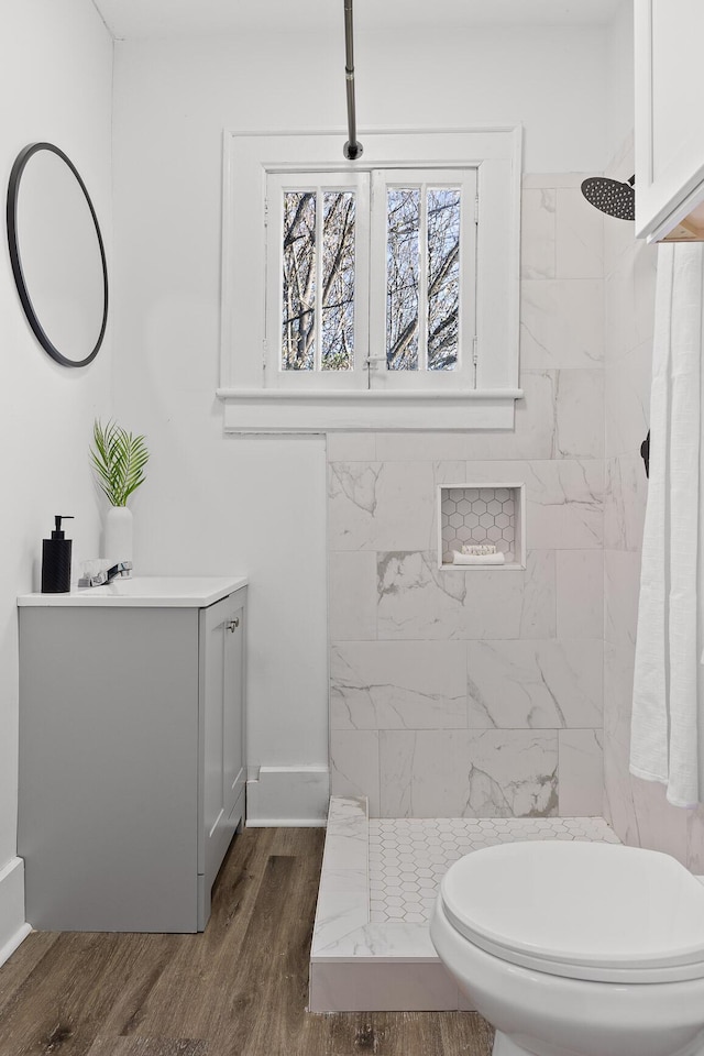 bathroom featuring toilet, vanity, wood-type flooring, and tiled shower