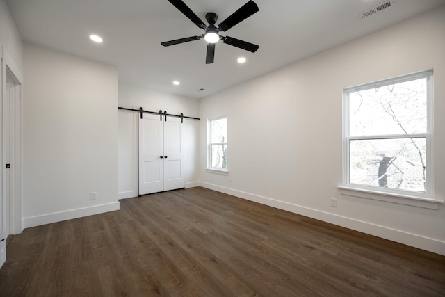 unfurnished bedroom with a barn door, multiple windows, dark wood-type flooring, and ceiling fan