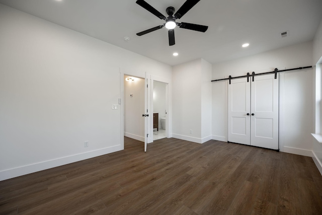 unfurnished bedroom featuring ceiling fan, a barn door, dark hardwood / wood-style flooring, and a closet