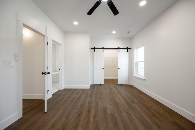 unfurnished bedroom featuring dark wood-type flooring, ceiling fan, a barn door, a spacious closet, and a closet