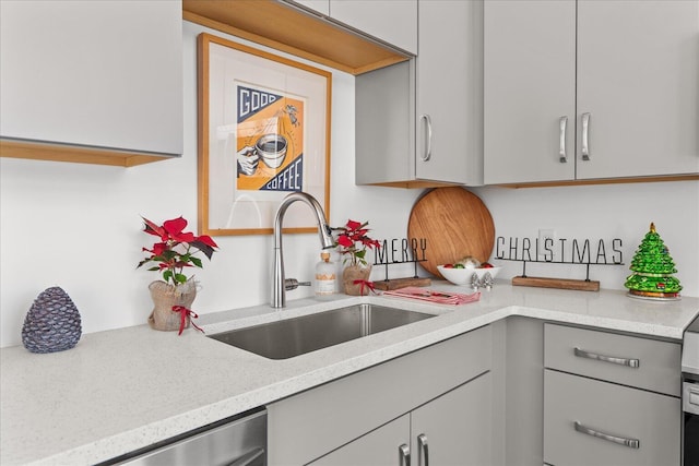 kitchen featuring light stone countertops, stainless steel dishwasher, gray cabinetry, and sink