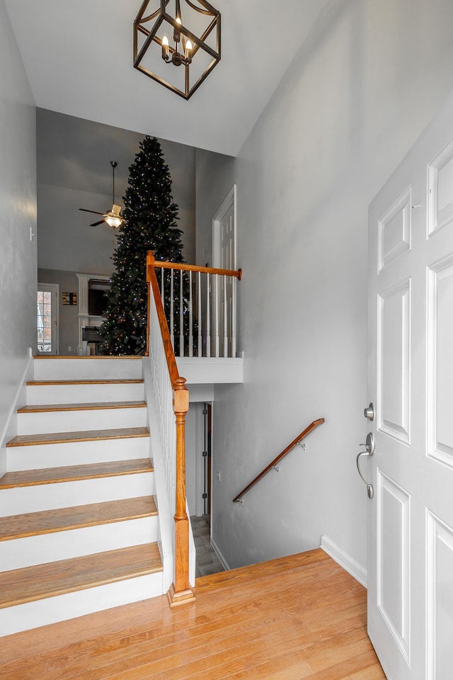 staircase with ceiling fan with notable chandelier and wood-type flooring