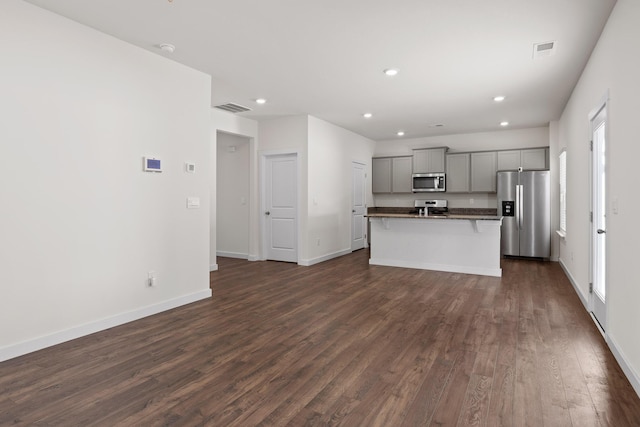 kitchen featuring dark wood-type flooring, appliances with stainless steel finishes, a center island with sink, and gray cabinetry