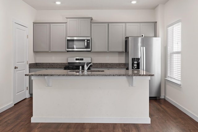 kitchen featuring appliances with stainless steel finishes, dark hardwood / wood-style flooring, gray cabinets, and an island with sink