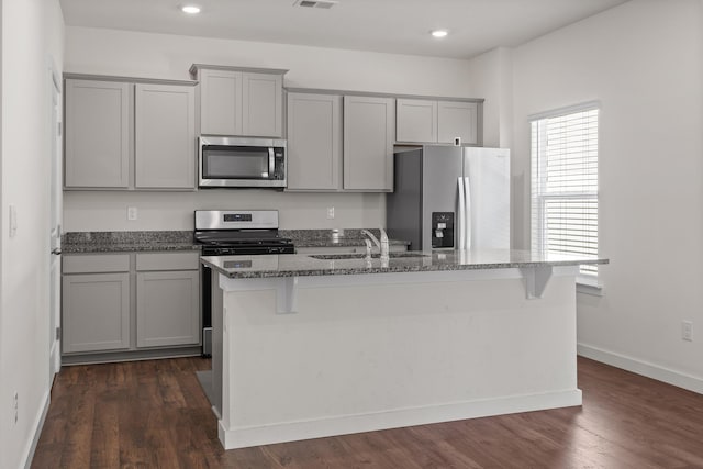 kitchen featuring appliances with stainless steel finishes, dark hardwood / wood-style flooring, gray cabinetry, and an island with sink