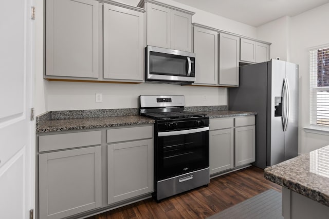 kitchen featuring dark hardwood / wood-style floors, gray cabinets, appliances with stainless steel finishes, and dark stone counters